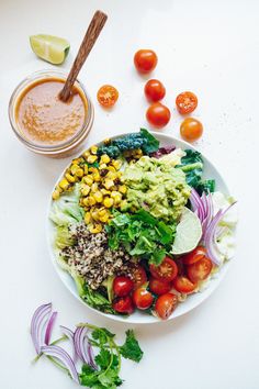 a white plate topped with a salad next to a bowl of dressing and sliced tomatoes