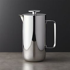 a stainless steel pitcher sitting on top of a table next to a black and white wall