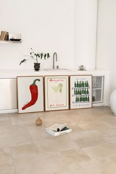 three framed art pieces sitting on the floor in front of a kitchen sink and counter