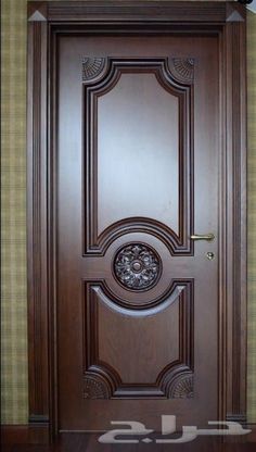 a wooden door with an ornate design on the top and bottom panel, in front of a green wall