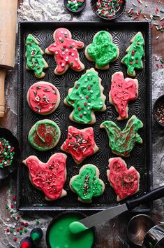 christmas cookies decorated with icing and sprinkles on a cookie sheet next to other holiday decorations