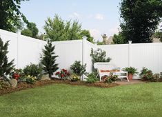 a white bench sitting in the middle of a garden next to a tall white fence