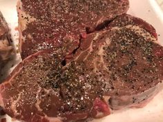 two pieces of steak covered in seasoning on top of a white plate next to another piece of meat