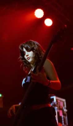 a woman holding a guitar in front of red lights