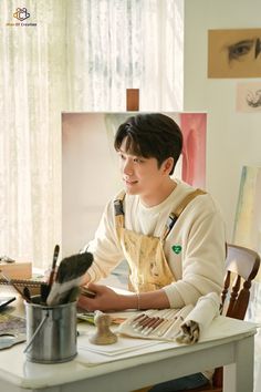 a young man sitting at a table in front of an easel