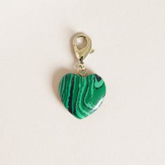 a green and black heart shaped charm on a white surface with a gold hook in the middle