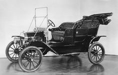 an old fashioned car sitting on top of a hard wood floor in front of a white wall