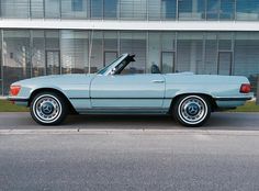 a light blue convertible car parked in front of a building with its open top down