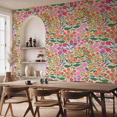 a dining room with colorful wallpaper and wooden chairs in front of a table surrounded by vases