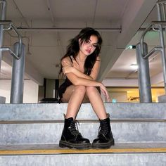 a woman sitting on some steps with her legs crossed and looking at the camera while wearing black boots