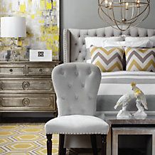 a bedroom with yellow and gray decor, white bedding and two chairs in front of the bed