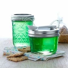 two mason jars filled with green liquid next to crackers