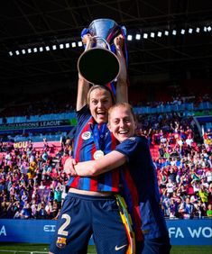 two women are holding up a trophy in front of a stadium full of people and fans