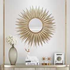 a gold starburst mirror on the wall above a dresser with books and vase