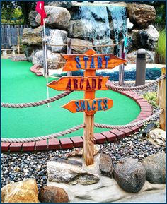 a sign that says start arcade slides in front of a miniature golf course and waterfall