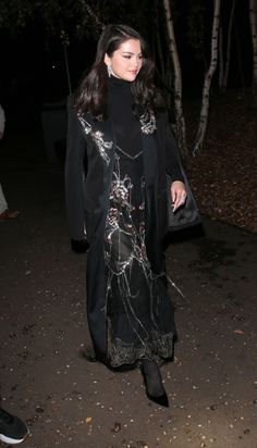 a woman is walking down the street at night wearing a long coat and black dress