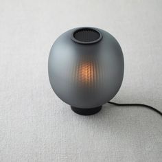 a gray speaker sitting on top of a white carpeted floor next to a black cord