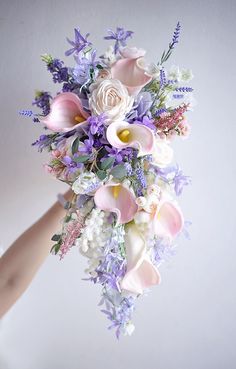 a bridal bouquet with pink, purple and white flowers is held by a woman's hand