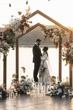 a bride and groom standing in front of an outdoor ceremony arch with flowers on it