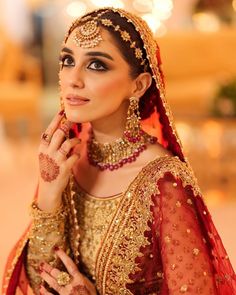 a woman in a red and gold bridal outfit with jewelry on her head, posing for the camera