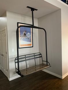 a metal swing hanging from the ceiling in a room with hardwood floors and white walls