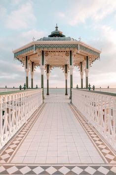 an ornate gazebo with tiled flooring and white tiles on the ground, in front of a cloudy sky