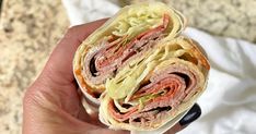 a hand holding a sandwich with meat and lettuce on it in front of a marble counter top