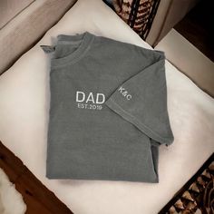 "These embroidered Dad T-shirts make a great Father's Day gift! Customized with the year they became a dad and the kids initials on the sleeve! **If you would like this shirt customized beyond adding the est. year and initials on the sleeve, please email us first to make sure that the changes are possible. There will be a $10 charge for extra customization outside of est. year and initials. We will then let you know to pick the \"extra customization\" option in the color selection in the size you need. When doing this please put the color shirt you would like from the available options in the personalization box along with your other customizations.**  ORDERING & SHIPPING *Your item will be shipped within 5-7 business days. *Please allow 2-5 business days to receive your item, more time ma Dad Shirts Father's Day, Personalized Cotton T-shirt For Father's Day, Father's Day Personalized Cotton T-shirt, Custom Text Cotton Tops For Personalized Gift, Cotton T-shirt With Letter Embroidery For Gift, Cotton T-shirt With Letter Embroidery As Gift, Personalized Cotton T-shirt With Custom Text, Personalized Cotton T-shirt With Letter Print, Personalized Cotton T-shirt With Short Sleeves