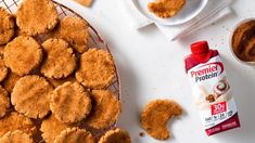 some cookies are sitting on a wire rack next to a bottle of peanut butter and two cups of milk