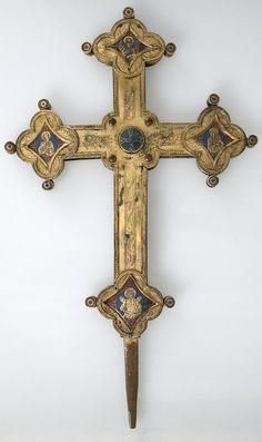 an ornate gold cross with blue and red designs on the sides, hanging from a white wall