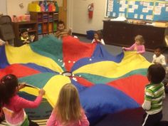 children are sitting on the floor and playing with a large parachute in a class room