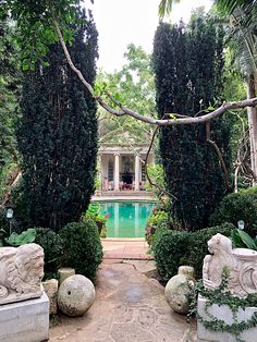 an outdoor garden with stone sculptures and pool surrounded by trees, shrubs and shrubbery