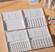 four white plastic keyboards sitting on top of a wooden table next to paint tubes and markers