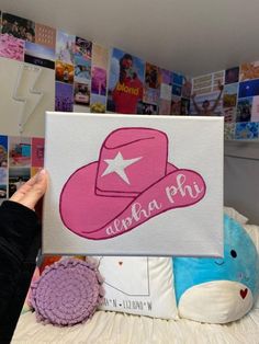 a person holding up a pink hat on top of a bed with pictures behind it