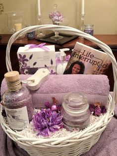 a white basket filled with purple flowers and personal care items next to a candle on a table