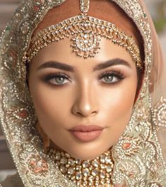 a woman wearing a bridal veil and headpiece with jewelry on her face, in front of a brick wall