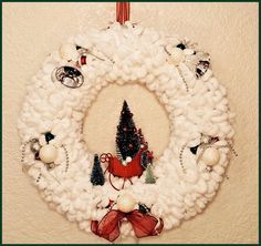 a knitted wreath hanging on the wall with ornaments around it and a christmas tree