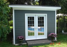 a small gray shed with two doors and flowers in the window boxes on the side