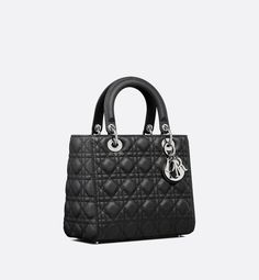 The Lady Dior bag epitomizes the House's vision of elegance and beauty. Sleek and refined, the timeless style is crafted in black grained calfskin with Cannage stitching, creating the instantly recognizable quilted texture. Silver-finish metal D.I.O.R. charms offer elegant appeal. Featuring a thin removable leather shoulder strap, the medium Lady Dior bag can be carried by hand or worn crossbody.. Lady Dior Bag Black, Dior And I, Icon Shoes, Womens Designer Bags, Dior Book Tote, Small Lady, Christian Dior Couture, Dior Couture, Backpack Tote Bag