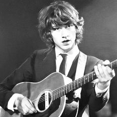 black and white photograph of a young man holding a guitar in his right hand while wearing a suit