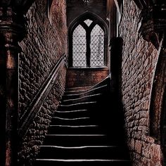 black and white photograph of stairs leading up to a window in an old building with stone walls