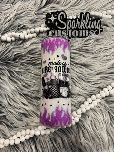 a purple and black spray bottle sitting on top of a gray rug next to a white beaded necklace