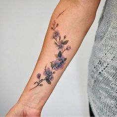 a woman's arm with purple flowers on the left side of her wrist and an arrow in the middle