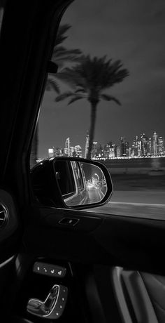 a view from inside a car looking at the city lights and palm trees in the distance