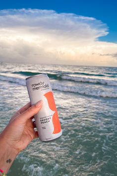 a person holding up a can of soda in front of the ocean with text that reads, rowdy mermaid lifestyle product photography