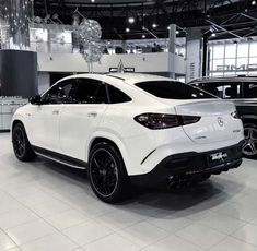 a white mercedes suv is on display in a showroom with other cars behind it