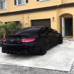 a black sports car parked in front of a yellow house with two garage doors open