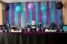 a table topped with lots of purple and blue decorations next to a wall covered in paper lanterns