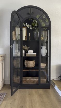 an arched glass cabinet in the corner of a room with wooden floors and white walls