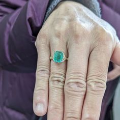 a close up of a person's hand wearing a ring with a green stone